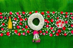 Songkran festival background with jasmine garland, flowers in water bowl, scented water and marly limestone for blessing on wet banana leaf background. photo