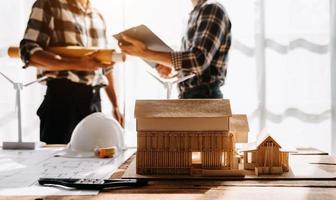 Professional team architect, engineer or interior reviewing blueprint on workplace desk behind house model in office photo