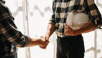 Engineers or architecture shaking hands at construction site for architectural project, holding safety helmet on their hands. photo
