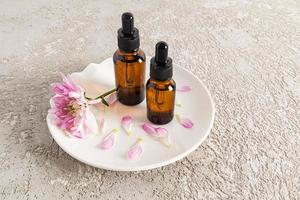 two glass bottles with a pipette with serum or oil for facial skin care stand on a white ceramic plate and a cement background. natural cosmetics. photo