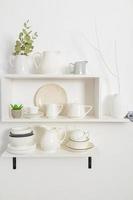 stylish white wooden shelves on a white textured wall with a set of dishes of their eco materials. beautiful design in a modern kitchen. photo