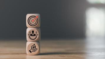 bloque de madera en la mesa, iconos de flecha que golpean el centro del objetivo del tablero de dardos, establecer objetivos comerciales y concepto enfocado, crecimiento y objetivos corporativos, planificación de estrategias de marketing