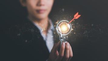 light bulb in businessman hand and arrow icon hitting center of dartboard target,Setting business goals and focused concepts, Organizational growth and objectives, marketing strategy planning photo