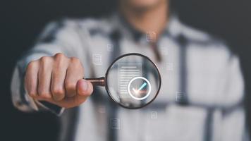 Businessman holding a magnifying glass, showing Audit Document concept,quality assessment management With a checklist, business document evaluation process, market data report analysis and consulting photo