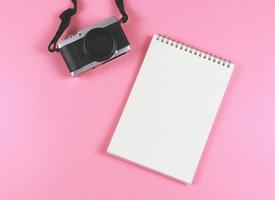 flat lay of blank page opened notebook and camera on pink background. photo