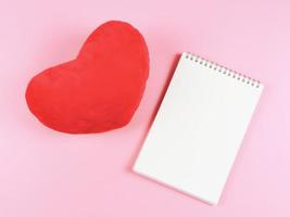 flat lay of opened  notebook with red heart shape pillow  on pink background with copy space. Love, Valentine's day, memory. photo