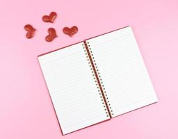 lat lay of opened red notebook or diary with red glitter hearts on pink background with copy space. Love, Valentine's day, memory. photo