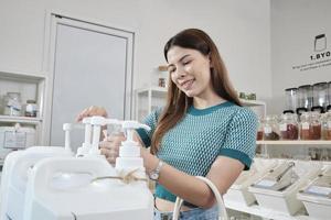 A Caucasian female customer pressed a reusable container to fill liquid products to recycle bottles at zero-waste and refill store, environment-friendly groceries, and sustainable shopping lifestyle. photo