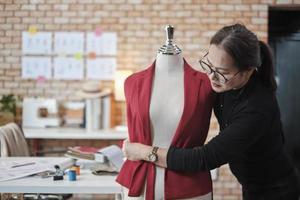 la diseñadora de vestuario asiática madura mide el tamaño de la forma de la marioneta de vestir en un estudio y trabaja con ropa, colección de diseño de moda, sastre boutique profesional, modista pyme emprendedora. foto