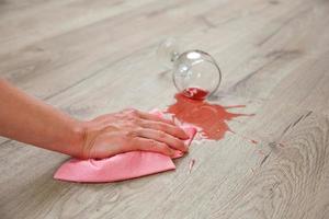 Glass of red wine fell on laminate, wine spilled on floor. A woman wipes the laminate from moisture. photo