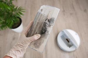 A woman holds a dust collector with garbage. The concept of a robot vacuum cleaner cleans the floors in the house. photo