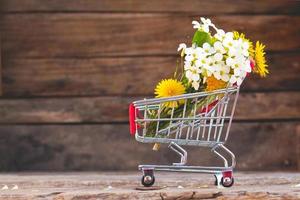 Shopping cart with flowers on the wooden background. photo