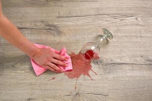 una copa de vino tinto cayó sobre el laminado, el vino se derramó en el suelo. una mujer limpia el laminado de la humedad. foto