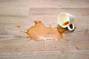 A cup of coffee fell on laminate, coffee spilled on floor. Focus on the puddle. photo