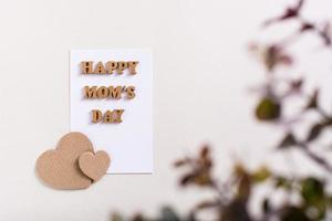 Happy mother's day. A sheet of paper with letters, cardboard hearts and a branch with leaves. photo