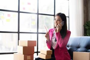 Startup small business SME, Entrepreneur owner using smartphone or tablet taking receive and checking online purchase shopping order to preparing pack product box. Selling online ideas concept photo