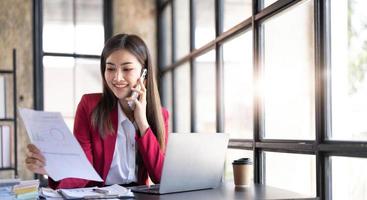 retrato de una joven y alegre mujer asiática de negocios que usa una aplicación de teléfono inteligente en la oficina del lugar de trabajo, concepto de empleado de una pequeña empresa independiente en línea de mercadeo en línea de telemercadeo de comercio electrónico. foto