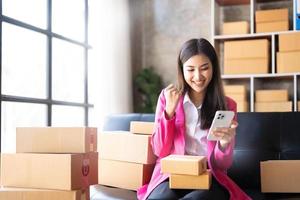 Startup SME small business entrepreneur of freelance Asian woman using a laptop with box Cheerful success happy Asian woman her hand lifts up online marketing packaging and delivery SME idea concept photo