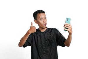 Asian man wearing black training t-shirt, With a happy excited gesture while looking at the smartphone screen. Isolated by white background photo