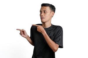 excited asian man wearing black training t-shirt, pointing to copy space. Isolated by white background photo