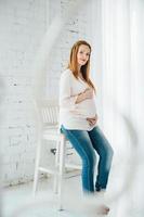 a red-haired pregnant girl in a light blouse and blue jeans photo