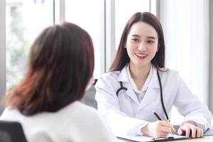 una doctora profesional asiática que usa abrigo médico habla con una paciente con su paciente mayor en la sala de examen, concepto de atención médica en la oficina del hospital.