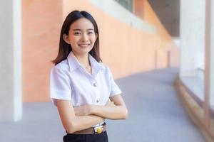 retrato joven asiática hermosa y bonita estudiante tailandesa en uniforme está sonriendo mirando a la cámara y con los brazos cruzados para presentar algo con confianza en el fondo de la universidad foto