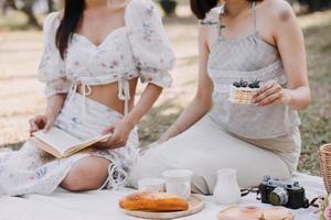 jovencitas gemelas morenas sentadas en el césped con las piernas ligeramente dobladas en las rodillas y mirando en un libro marrón, usando un abrigo casual en el clima soleado de otoño en un fondo borroso. foto