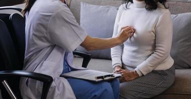 Homecare nursing service and elderly people cardiology healthcare. Close up of young hispanic female doctor nurse check mature caucasian man patient heartbeat using stethoscope during visit photo