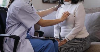 Homecare nursing service and elderly people cardiology healthcare. Close up of young hispanic female doctor nurse check mature caucasian man patient heartbeat using stethoscope during visit photo