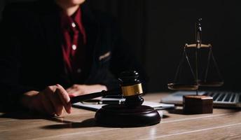 concepto de justicia y derecho. juez masculino en una sala de audiencias con el mazo, trabajando con computadora y teclado de acoplamiento, anteojos, en la mesa a la luz de la mañana foto