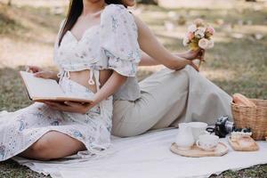 jovencitas gemelas morenas sentadas en el césped con las piernas ligeramente dobladas en las rodillas y mirando en un libro marrón, usando un abrigo casual en el clima soleado de otoño en un fondo borroso. foto