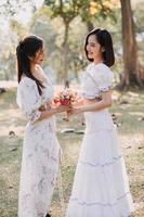 Young pretty brunette twin girls sitting on the grass with legs slightly bent in knees and looking in a brown book, wearing casual coat in autumn sunny weather on blurry background. photo