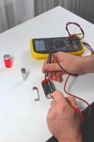 man measuring battery charge with digital multimeter photo