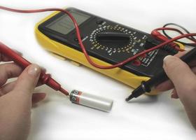 a man measures the charge of the battery with a digital multimeter on a white background photo