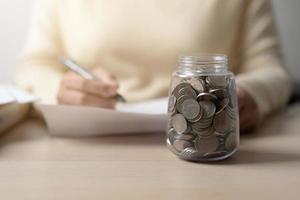 mujer trabajadora y un frasco lleno de monedas tailandesas. concepto de trabajar duro ahorrando más. foto