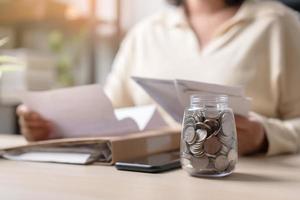 Working woman and a jar full with Thai currency coins. Concept of work hard saving more. photo