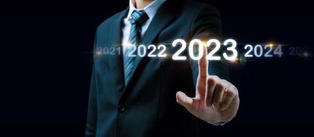 2023. mano de hombre de negocios tocando y señalando el año 2023 con pantalla virtual sobre fondo oscuro, meta, cambio de 2022 a 2023, estrategia, inversión, planificación empresarial, concepto de feliz año nuevo foto