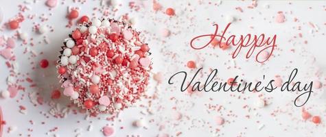 Valentine. Cake on a plate in the shape of a heart on a pink background. Valentine background.  Lettering Happy Valentine's Day. Banner. photo