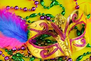 Carnival mask with feathers on yellow background. Multicolored beads Mardi Gras or Fat Tuesday symbol. photo