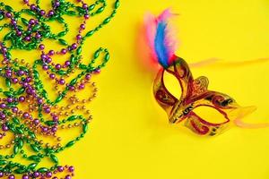 Multicolored beads and carnival mask on yellow background. Mardi Gras concept. Fat Tuesday symbol. photo