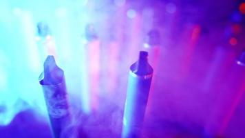 Lots of E-cigarettes and Vapes in Neon Lighting and Smoke. Concept of Bad Habits. Modern Alternative to Tobacco Products. Nicotine Addiction. Slow Motion. video