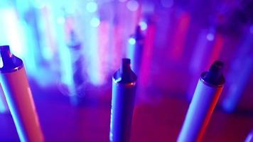 Lots of E-cigarettes and Vapes in Neon Lighting and Smoke. Concept of Bad Habits. Modern Alternative to Tobacco Products. Nicotine Addiction. Slow Motion. video