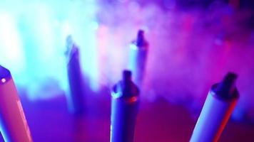 massor av e-cigaretter och vapes i neon belysning och rök. begrepp av dålig vanor. modern alternativ till tobak Produkter. nikotin missbruk. långsam rörelse. video