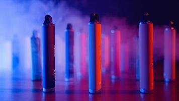 veel van e-sigaretten en vapen in neon verlichting en rook. concept van slecht gebruiken. modern alternatief naar tabak producten. nicotine verslaving. langzaam beweging. video