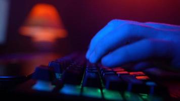close-up, homem irreconhecível usando um teclado de computador para codificar um site na iluminação neon. hacker e cibercrime ou conceito de ciberespaço. video