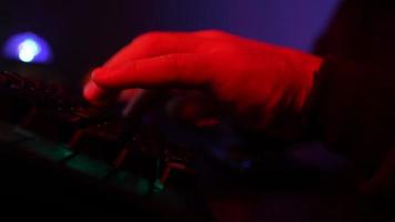 mãos masculinas digitando em um teclado de computador em iluminação neon. cara irreconhecível trabalhando em um laptop à noite. conceito de hackers e crimes cibernéticos ou ciberespaço. video