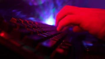 avvicinamento, irriconoscibile uomo utilizzando un' computer tastiera per codice un' sito web nel neon illuminazione. pirata e crimine informatico o cyberspazio concetto. video