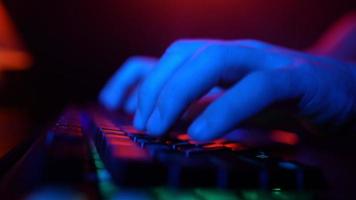 maschio mani digitando su un' computer tastiera nel neon illuminazione. irriconoscibile tipo Lavorando su un' il computer portatile a notte. concetto di gli hacker e informatica crimini o cyberspazio. video