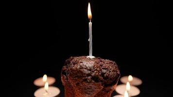 muffin de chocolate com uma vela acesa em um fundo preto. conceito de serviços memoriais e religião. video